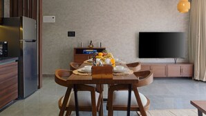Ett modernt kök med ett inbyggt kylskåp, en matplats med ett träbord och stolar, en platt-TV och ett litet skåp.