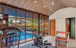 A gym with exercise equipment, large windows, and a view of a swimming pool. - Chic 1bhk in Candolim Pool Gym Near Beach (Candolim)