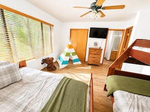 A bedroom with a bed, a wooden dresser, a television, and a ceiling fan.