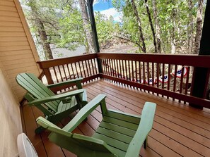Una terraza de madera con dos sillas Adirondack verdes, un muro de piedra y vistas a árboles y un cielo despejado.