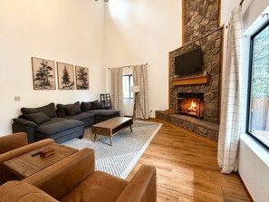 Una sala de estar con chimenea de piedra, un sofá grande, una mesa de centro y un televisor montado en la pared.