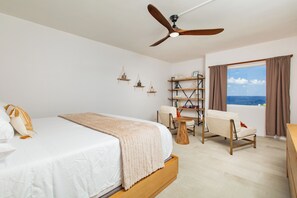 A bedroom with a bed, a ceiling fan, a window with curtains, a chair, and a small table. - Oceanview Condo, Pool, Parking-Beaches &Island attractions minutes away (Christiansted)