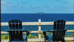 Duas cadeiras Adirondack de frente para uma cerca de madeira, com vista para o oceano e uma ilha distante.