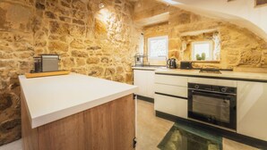 A kitchen with a stone wall, white countertop, wooden cabinets, and a built-in oven. - Charming House of Character in Victoria Gozo (Victoria)