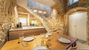A stone-walled dining area with a wooden table set for two, a staircase, and a fire exit sign. - Charming House of Character in Victoria Gozo (Victoria)