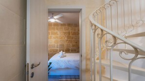 A room with a bed, a ceiling fan, a checkered rug, and a staircase with ornate railings. - Charming House of Character in Victoria Gozo (Victoria)