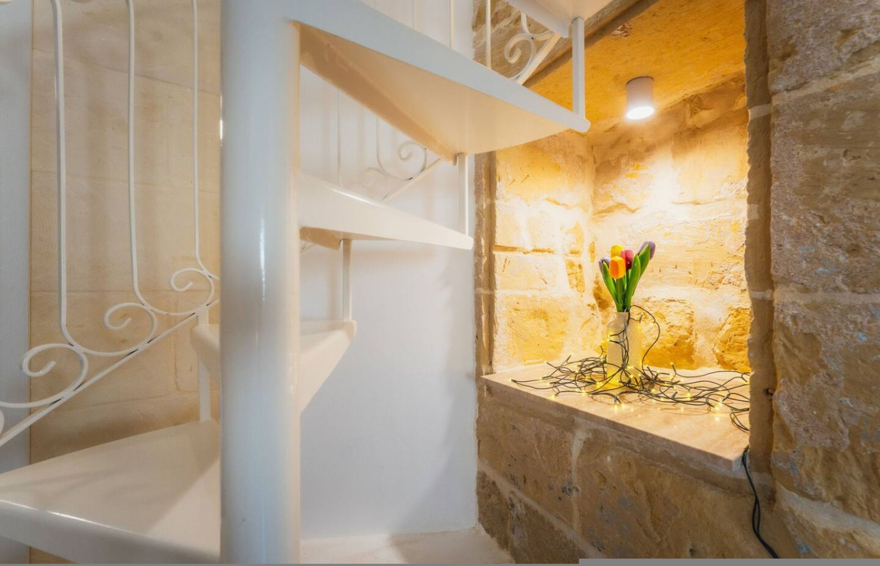 A room with a stone wall, a white metal staircase, and a vase with flowers on a ledge.