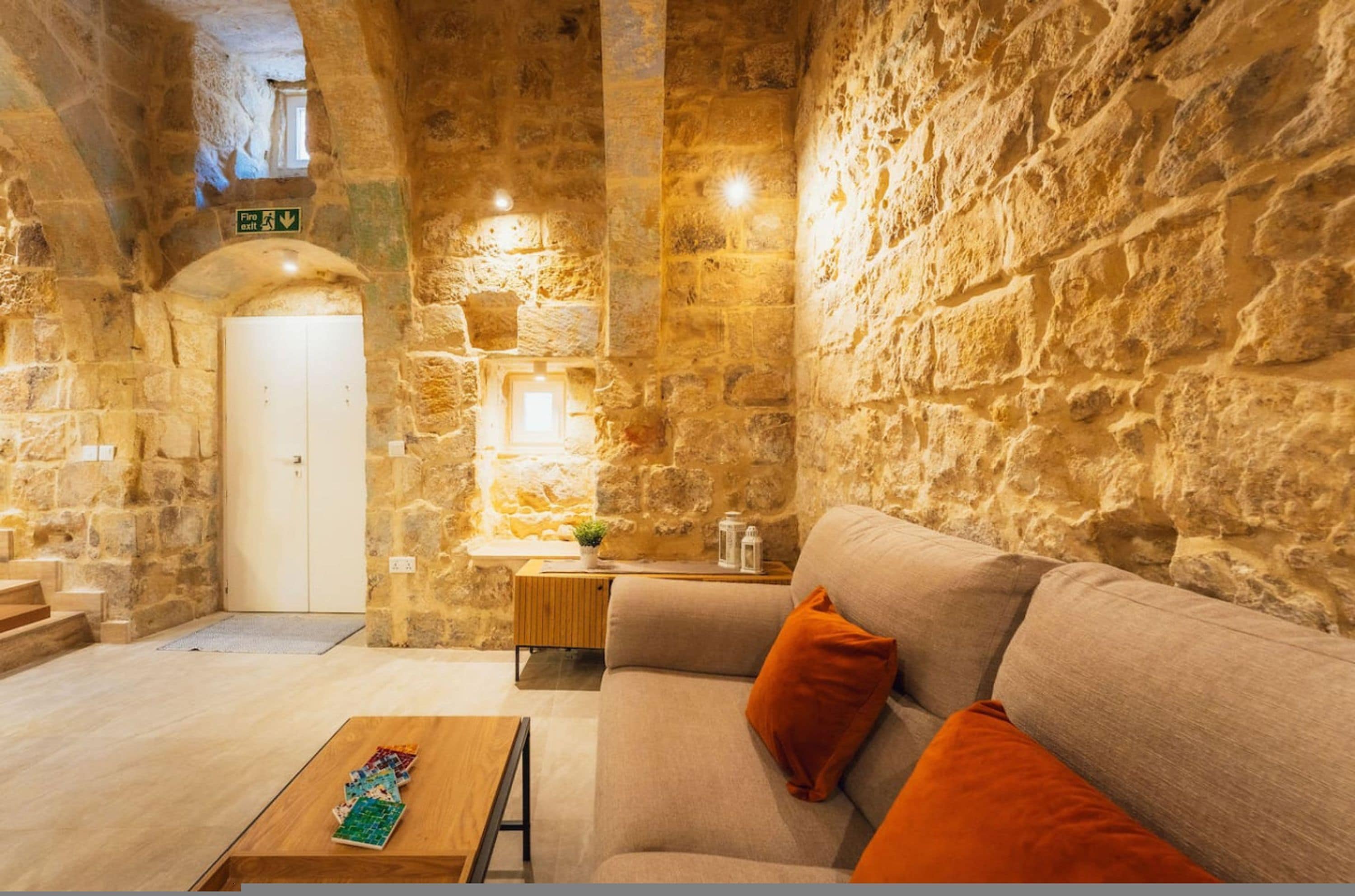 A stone-walled room with a sofa, a coffee table, and a door marked 'Fire Exit.'