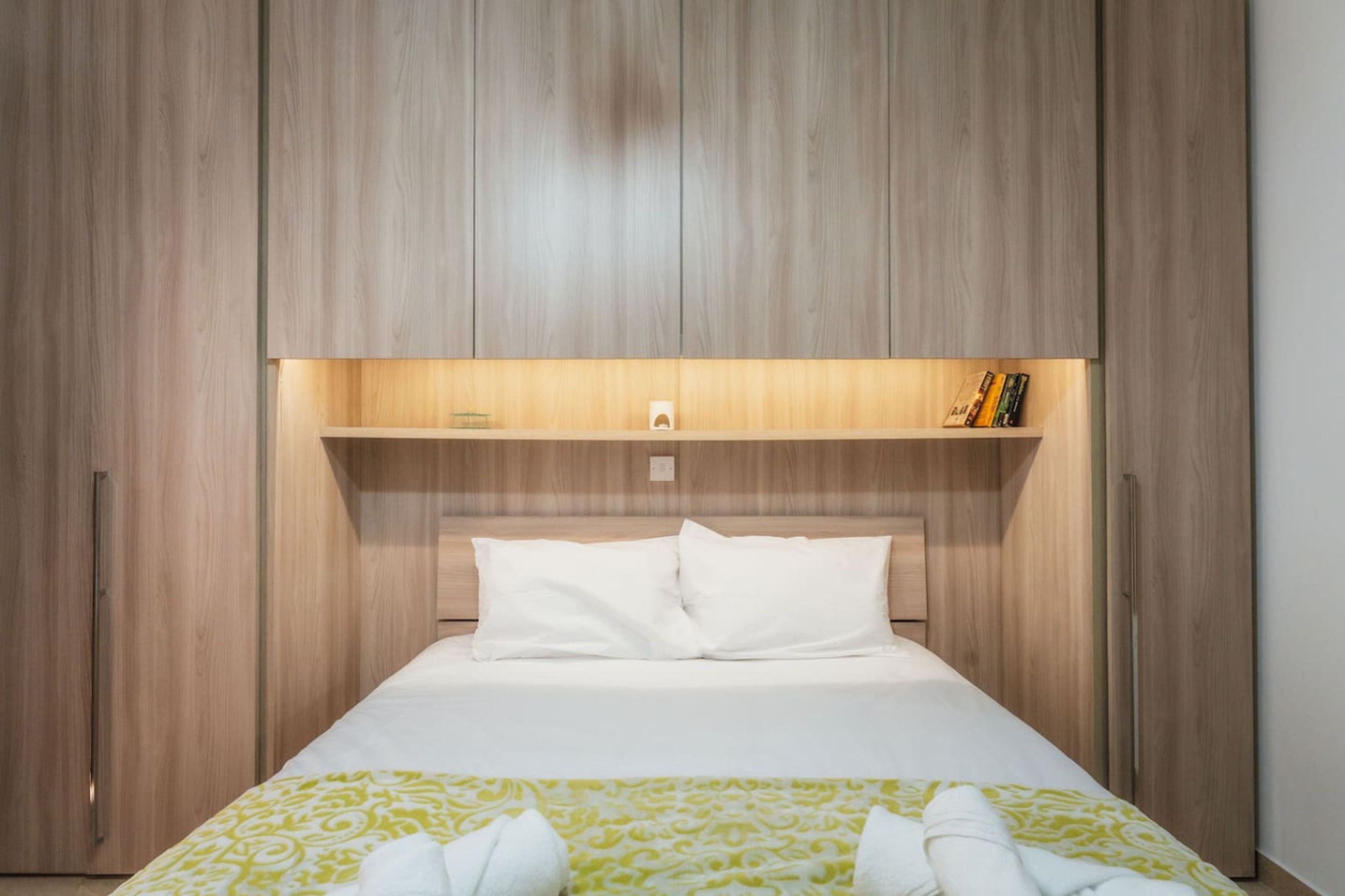 A hotel room with a large bed, wooden wardrobe, and a shelf with books.