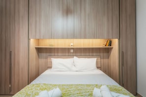 A hotel room with a large bed, wooden wardrobe, and a shelf with books. - Marsalforn Apartment Walk to Beach Seaside Living (Zebbug)