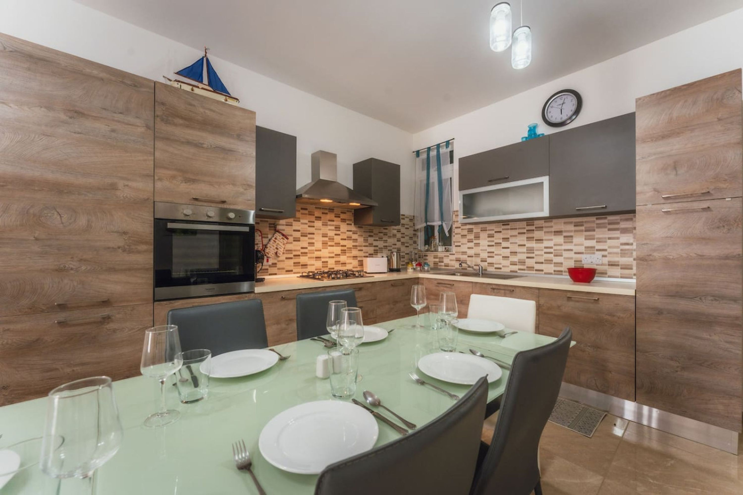 A modern kitchen with wooden cabinets, a built-in oven, and a dining area with a table set for four.