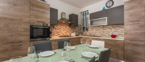A modern kitchen with wooden cabinets, a built-in oven, and a dining area with a table set for four.