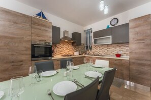 A modern kitchen with wooden cabinets, a built-in oven, and a dining area with a table set for four. - Marsalforn Apartment Walk to Beach Seaside Living (Zebbug)