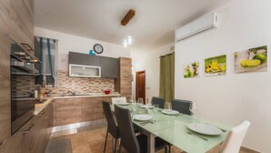A modern kitchen with a dining area, featuring a large island, built-in appliances, and a clock on the wall. - Marsalforn Apartment Walk to Beach Seaside Living (Zebbug)