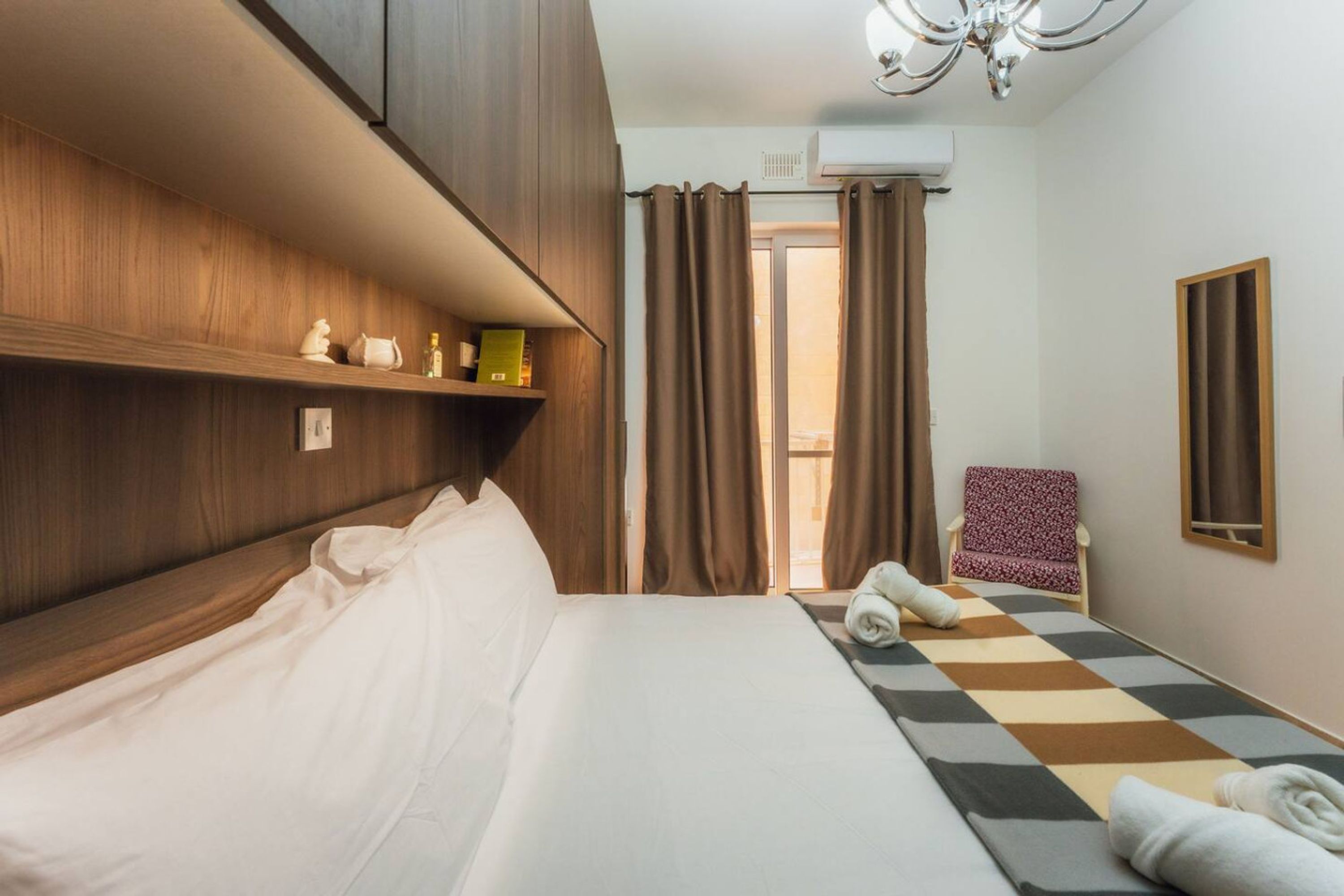 A hotel room with a bed, a chair, a mirror, and a window with curtains.