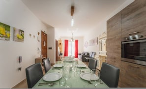 A dining area with a long table set for six, a kitchen with modern appliances, and a hallway leading to another room. - Marsalforn Apartment Walk to Beach Seaside Living (Zebbug)