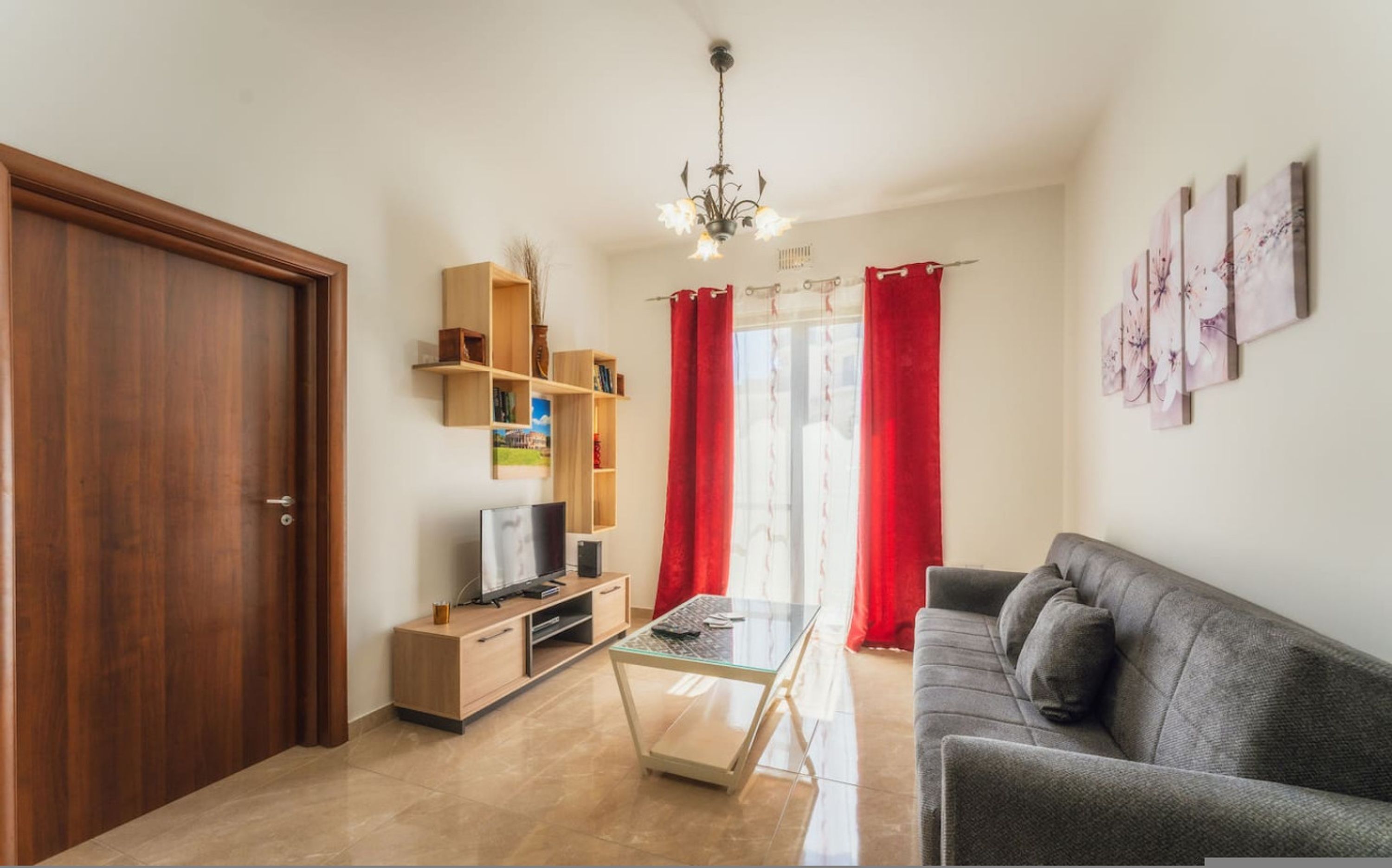 A living room with a sofa, TV, wooden shelves, and a glass coffee table.