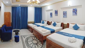 Une chambre d’hôtel avec trois lits, un lustre, des rideaux bleus et des œuvres d’art accrochées aux murs.