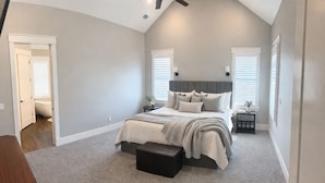 A bedroom with a bed, bedside tables, a nightstand, a bench, and a window with blinds.