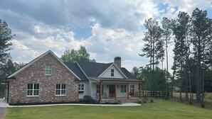 A two-story brick house with a covered porch, a well-maintained lawn, and a gravel driveway.