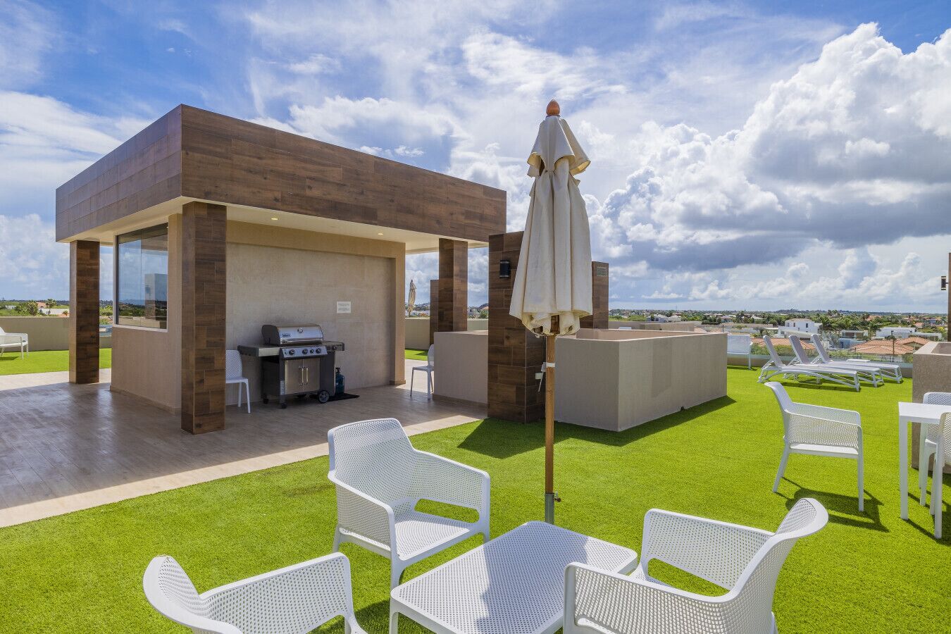 An outdoor patio with a barbecue area, white chairs, and a large umbrella.