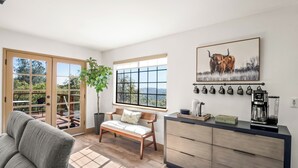 Ein modernes Wohnzimmer mit einer Couch, einer Bank, einer Kaffeestation und einem großen Fenster mit Blick auf die Stadt.
