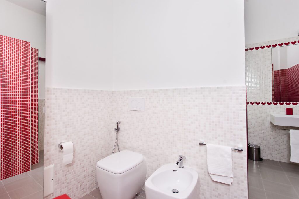Une salle de bain équipée de toilettes, d’un bidet et d’un miroir orné d’un cadre en forme de cœur rouge.