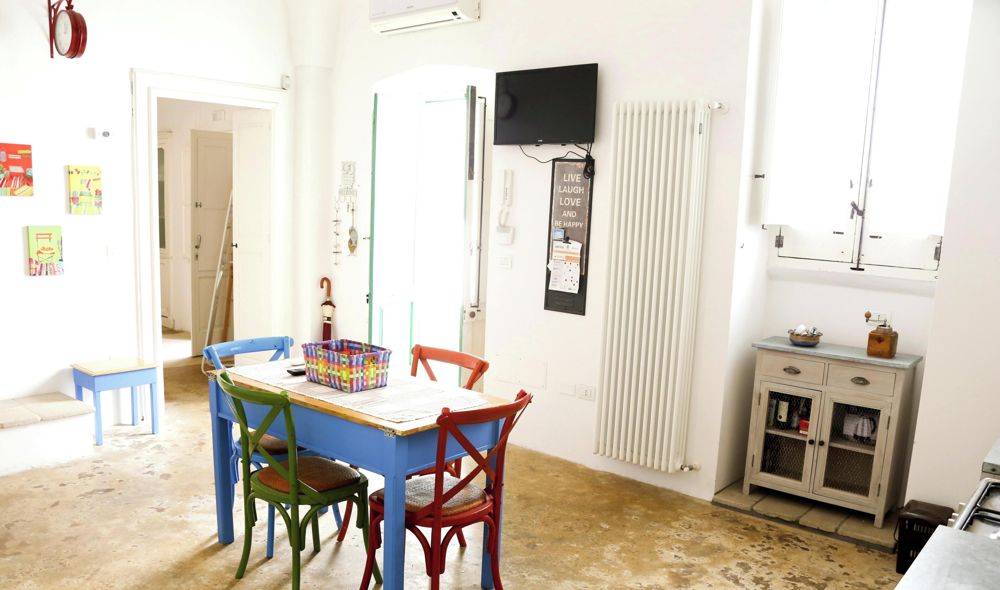 A dining area with a table, chairs, a clock, a television, and a radiator.