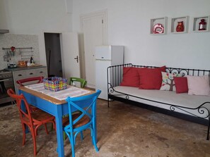 Un espace de vie compact comprenant un coin cuisine, une table à manger avec des chaises, un canapé avec des coussins et un réfrigérateur.