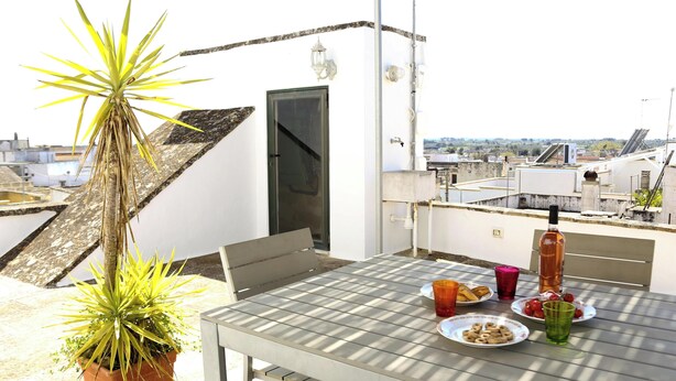 A rooftop terrace with a table set for two, a potted plant, and a city view. - Relais of Hearts with terrace (Matino)