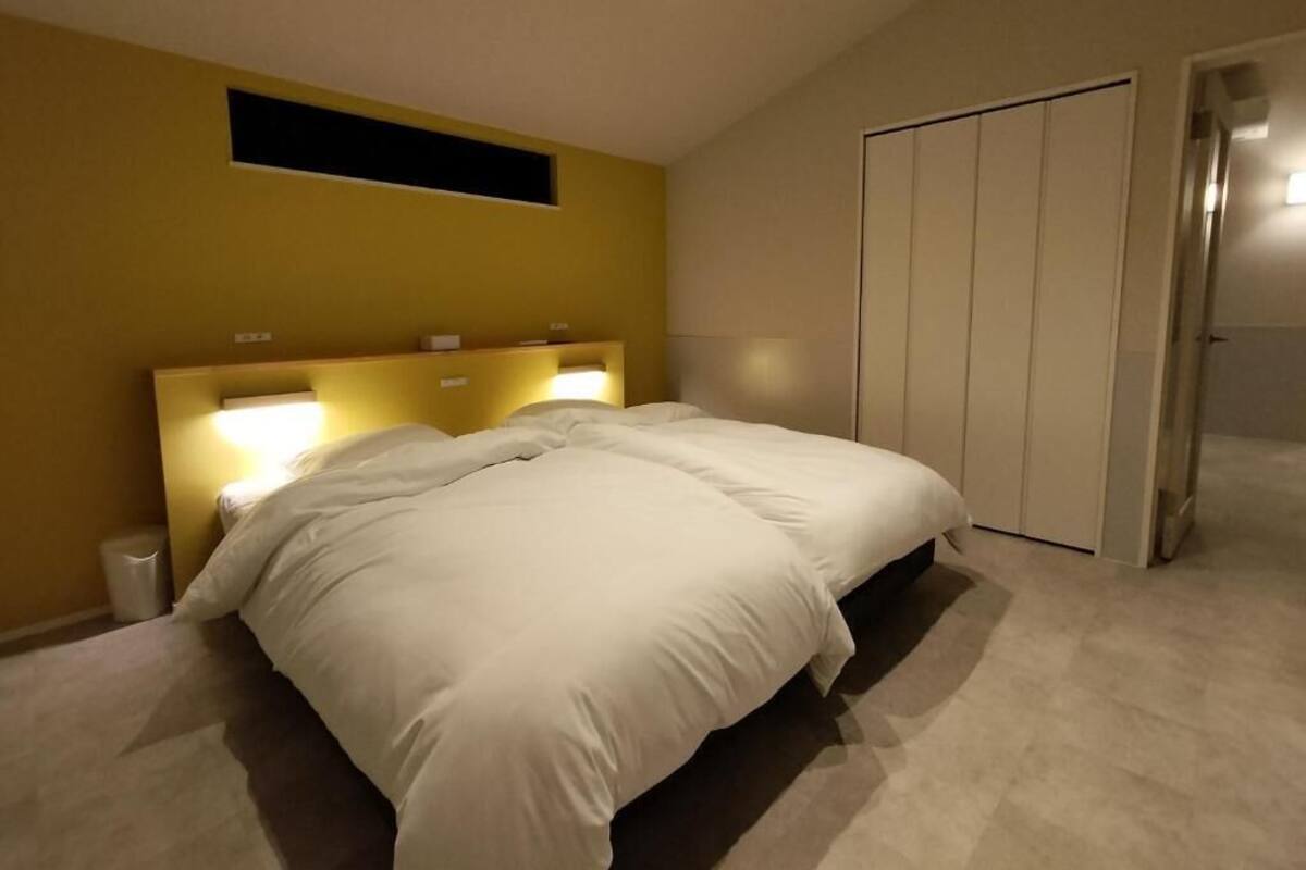 A bedroom with a bed, a bedside table, a wall-mounted light, and a wardrobe.