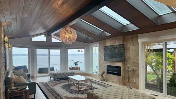 A spacious living room with a large window, a chandelier, a sofa, a coffee table, and a television. - Perfect 6-bedroom house in Blaine for your next getaway (Blaine)