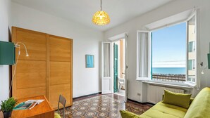Et værelse med et træskrivebord, en grøn sofa, et mønstret gulv, et vindue med havudsigt og en hængende lampe.