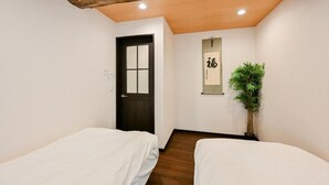 Een kamer met twee bedden, een houten plafond, een deur, een bordje aan de muur en een bloempot met plant.