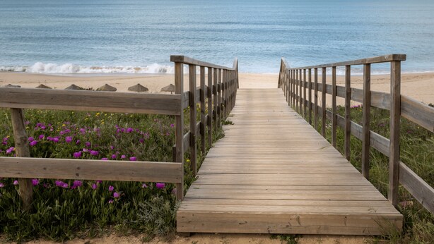 Un paseo marítimo de madera que conduce a una playa, con barandas de madera a ambos lados.