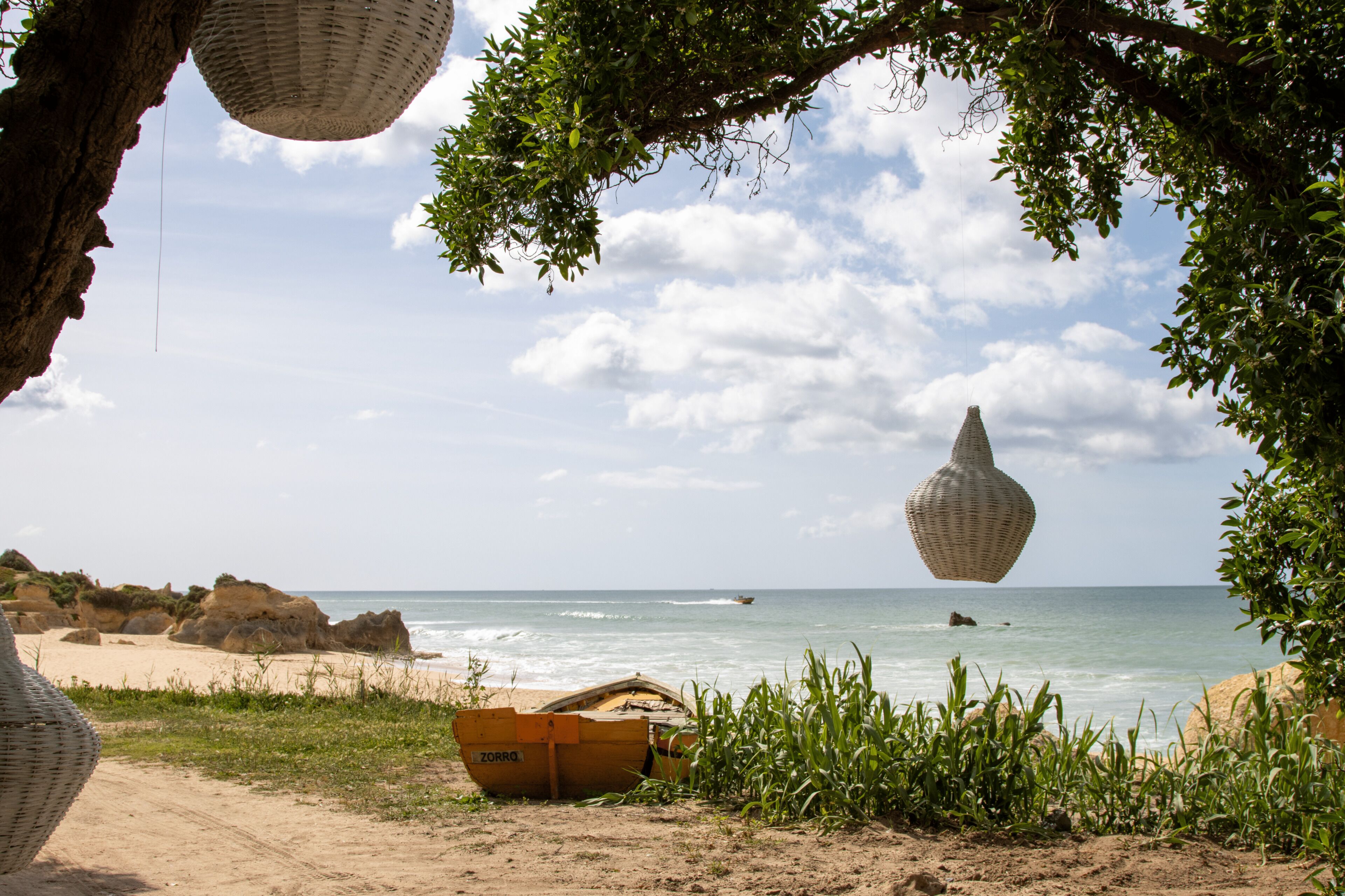Ein Strand mit einem Korbschiff, einer großen hängenden Korbstruktur und einem kleinen Boot im Wasser.