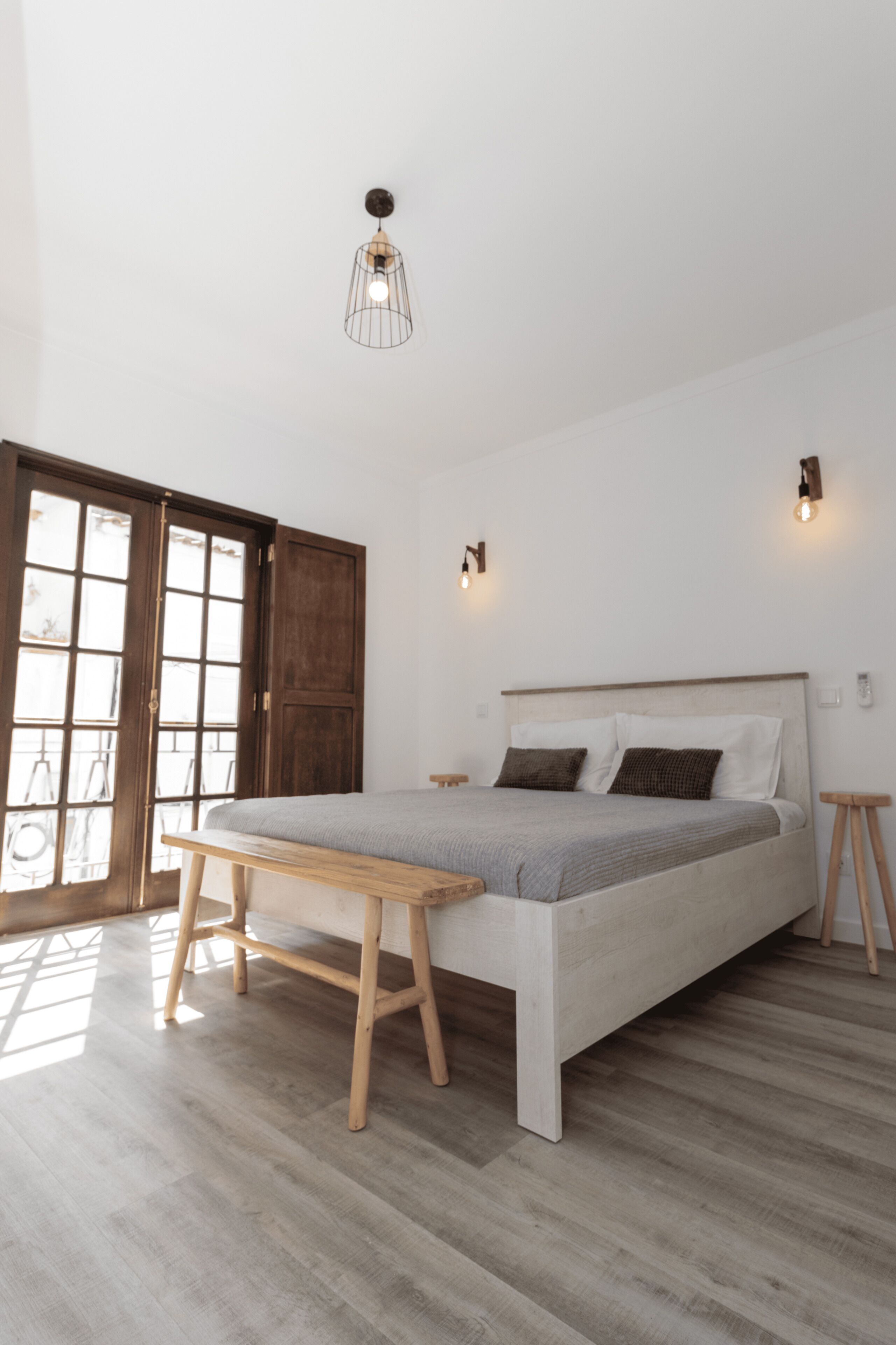 Een slaapkamer met een bed, houten vloer en een deur met glaspanelen.