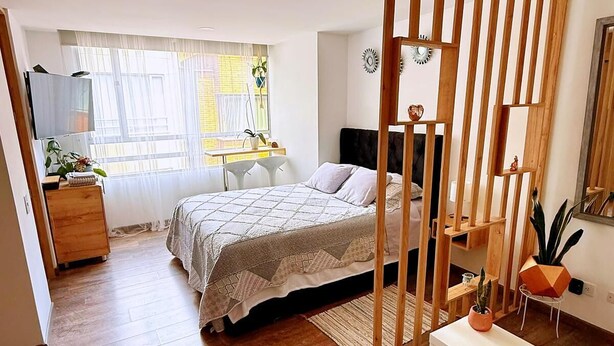 Ein Schlafzimmer mit Bett, Schreibtisch, Stuhl, kleinem Tisch und einem dekorativen Raumteiler.