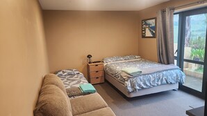 A bedroom with two beds, a sofa, a small table, and a window with a view.