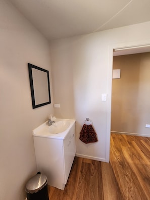 A bathroom with a white sink, a mirror, a towel ring, and a trash can. - Sugarloaf Studio with a view. Near Church Rd and Mission Estate Wineries (Napier)