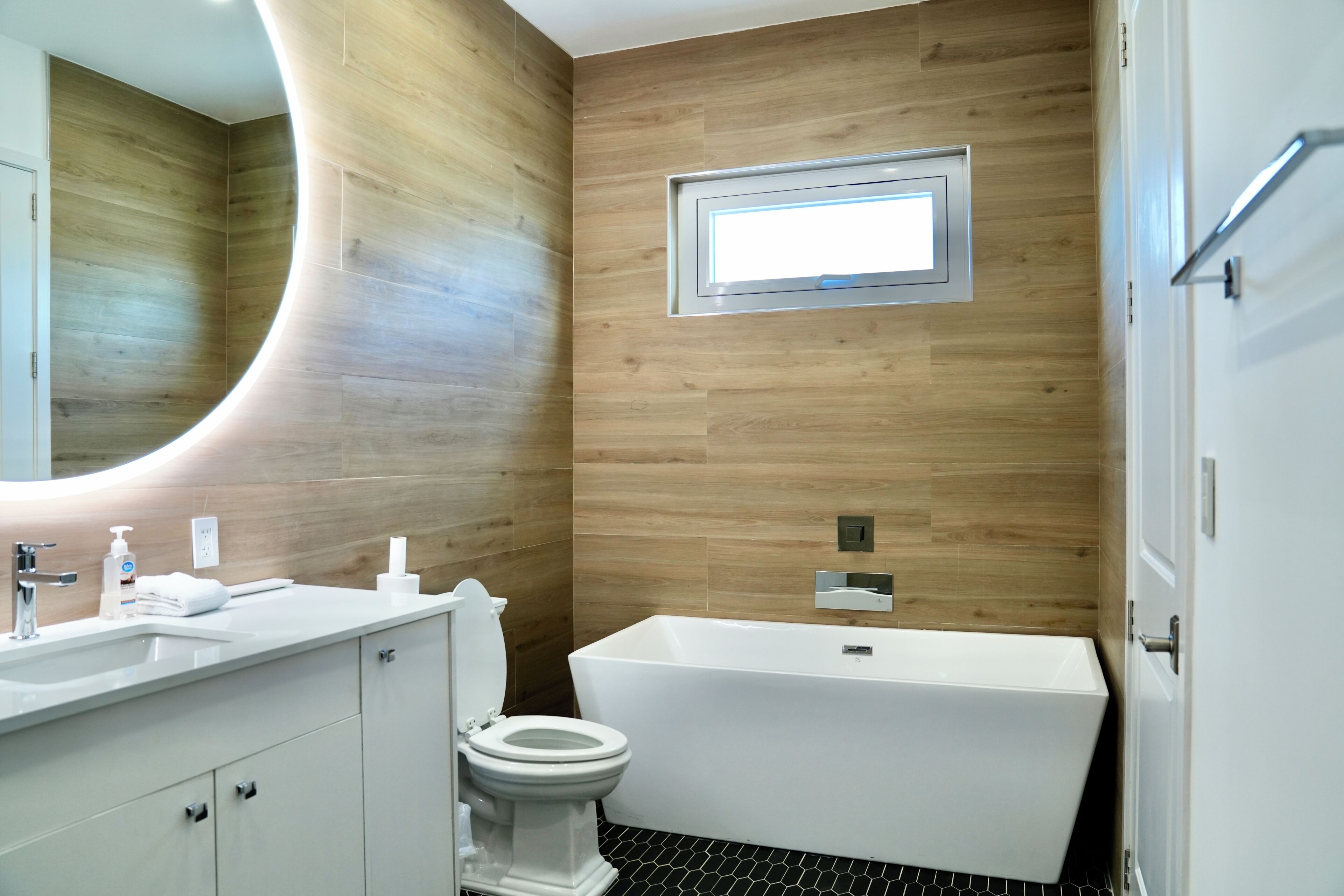A modern bathroom with a wooden wall, a white sink, a toilet, and a bathtub.