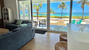 Una sala de estar con sofá, una mesa de comedor y vista a una playa con palmeras y el océano.