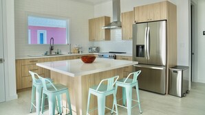Une cuisine moderne dotée d’un îlot central, d’appareils électroménagers en acier inoxydable et de meubles de rangement en bois clair.