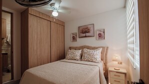 Ein Schlafzimmer mit einem Bett, einem Nachttisch, einer Lampe, einem Deckenventilator und Bildern an der Wand.