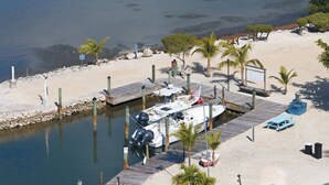 A marina with boats docked, a wooden pier, and a sandy beach with palm trees. - Tipsy Turtle -2 bed 3 bth Condo with Pool/ Dockage at Marina and gorgeous Gulf water views (Marathon)