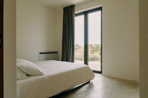 A bedroom with a bed, a nightstand, a window with curtains, and a view of trees. - Amurè Luxury Villa near Ostuni | Heated Infinity Pool & Privacy (Carovigno)