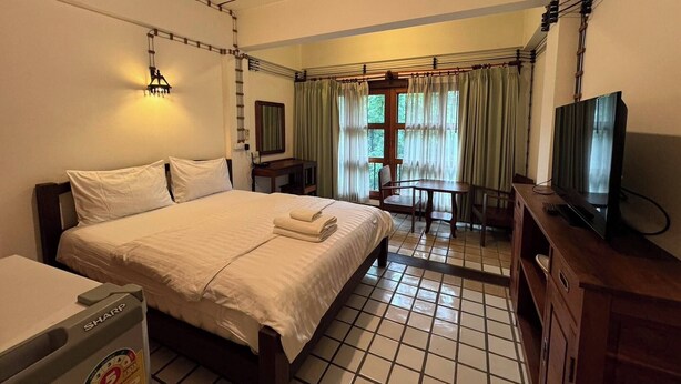 A hotel room with a bed, a desk, a television, and a window with curtains. - Room-204 Serene Teak Boutique Apartments (Chiang Mai)