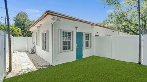 A single-story house with a white exterior, a blue door, and a small front yard with artificial grass. - Charming  Studio Apartment 1 in Fort Lauderdale.  (Fort Lauderdale)