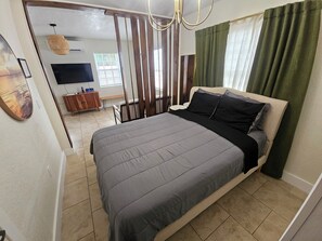 Ein Schlafzimmer mit einem Bett, einem Fernseher, einer Holzkommode und einem Fenster mit Vorhängen.