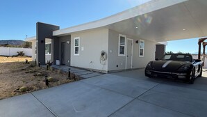 A modern house with a covered driveway, a black sports car, and a desert landscape. - 2-bedroom house in charming Joshua Tree with pool (Joshua Tree)